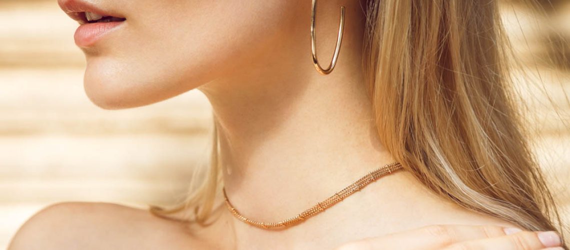 Close-up of a beautiful young blonde woman's neck without a shirt with gold earrings and a tiny gold choker.
